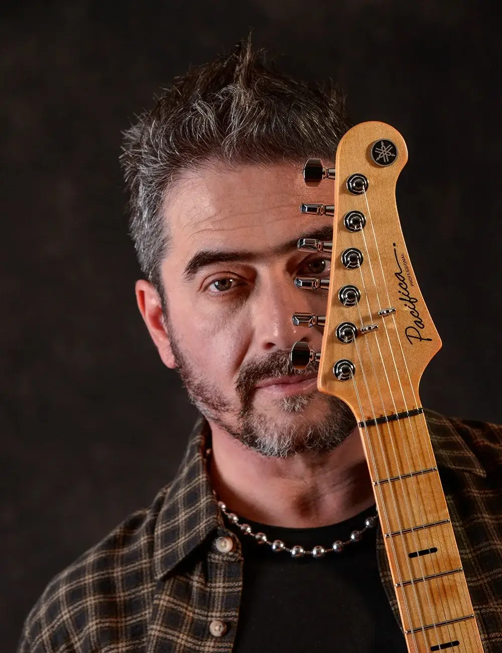 Tonio Ruiz con el clavijero de una guitarra Yamaha Pacifica frente al rostro